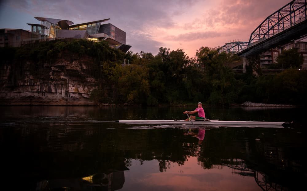 A sculler on the Tennessee River at dusk below the Hunter Museum and Walnut Street Bridge — Chattanooga's downtown riverfront